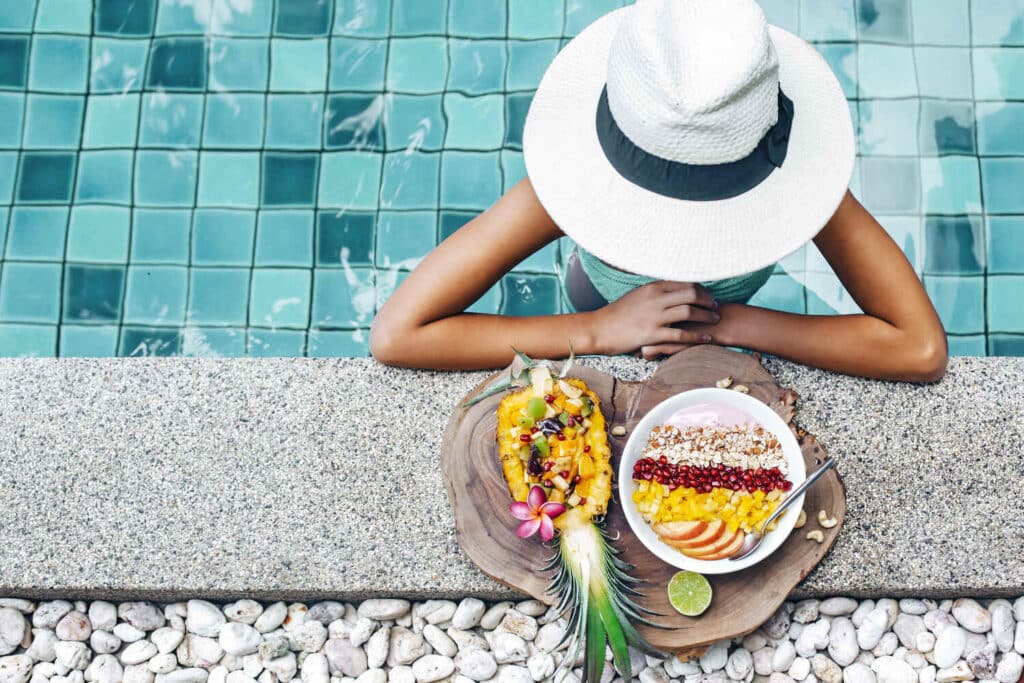 Girl relaxing and eating fruit plate by the hotel pool. Exotic summer diet. Tropical beach lifestyle.